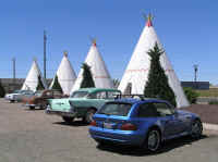 A bunch of old cars in front of cute motel rooms.